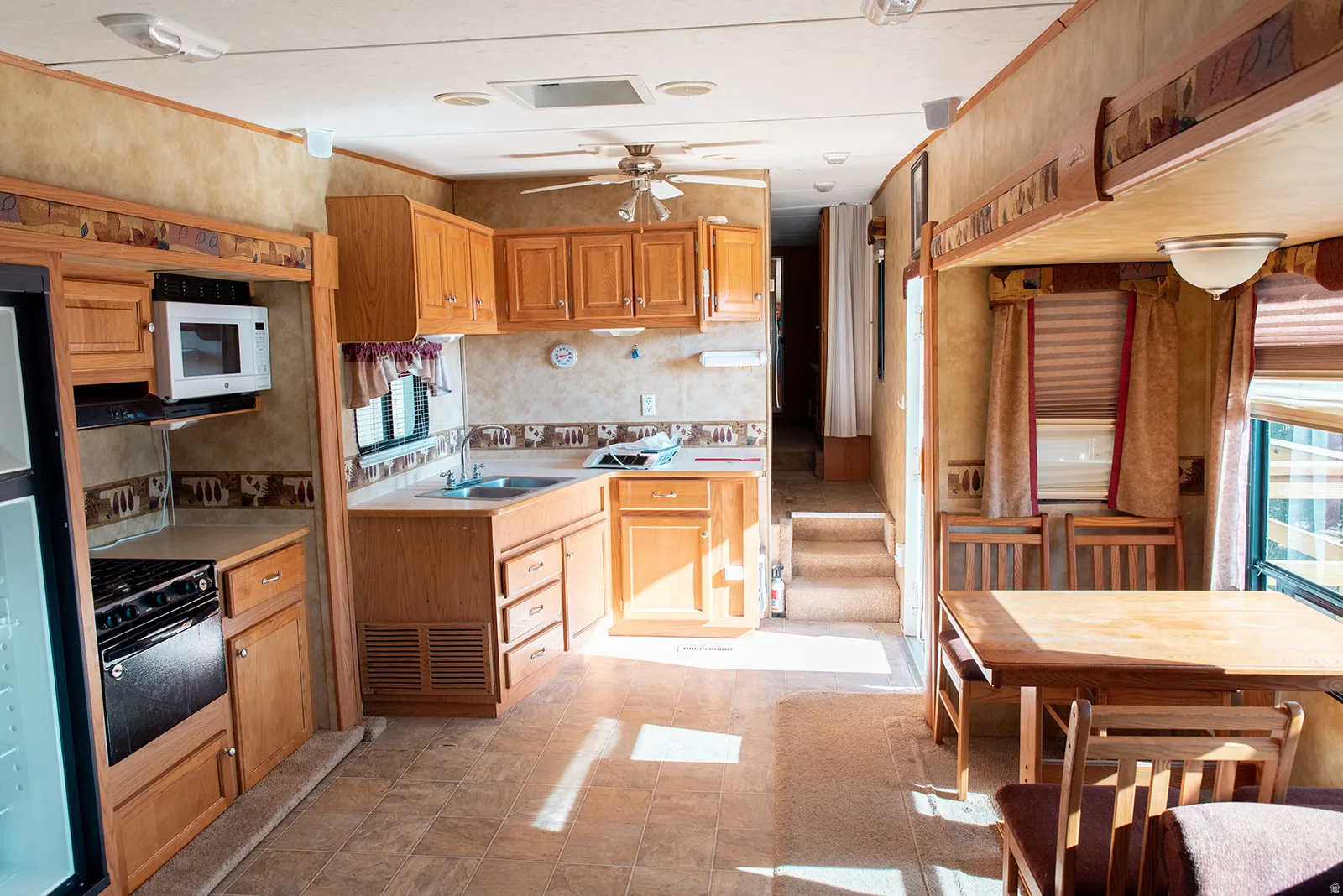 Kitchen with light countertops, white microwave, a ceiling fan, and wood finish cabinetry