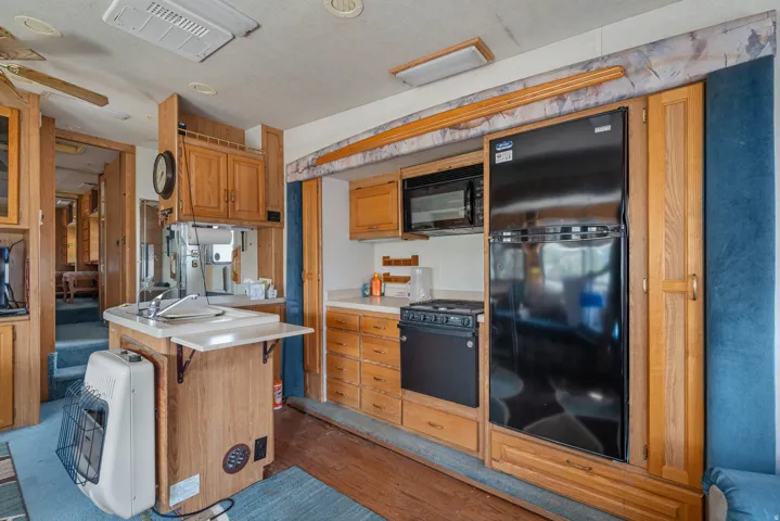 Wood-finish cabinetry, built-in black refrigerator, black microwave, and a compact range