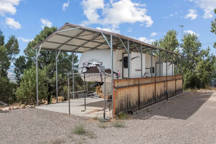 Metal-frame carport with a corrugated metal roof, concrete pad, and an attached privacy fence