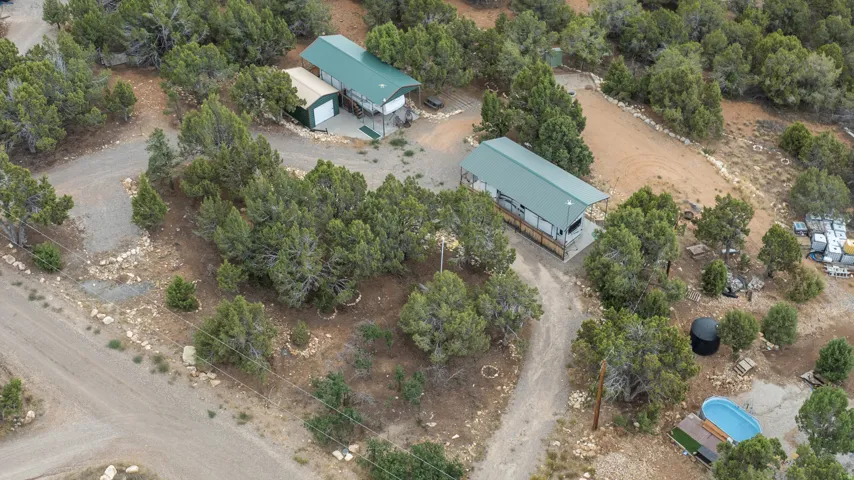Rural property featuring a main residence with a green metal roof, a secondary structure with a green metal roof and an extended covered porch, a detached garage, and extensive natural landscaping