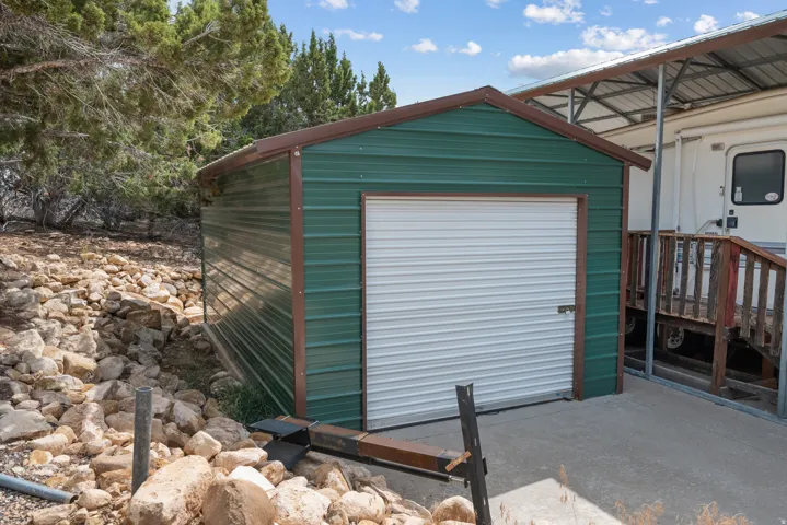 Green metal storage shed with a roll-up door, concrete pad, and surrounding natural rock landscaping