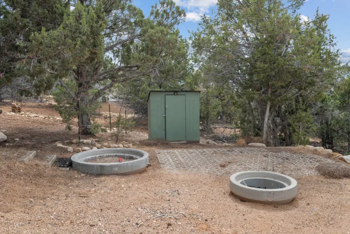 Outdoor utility shed with a metal roof and panel siding, two circular concrete fire pits, and a patterned paver base