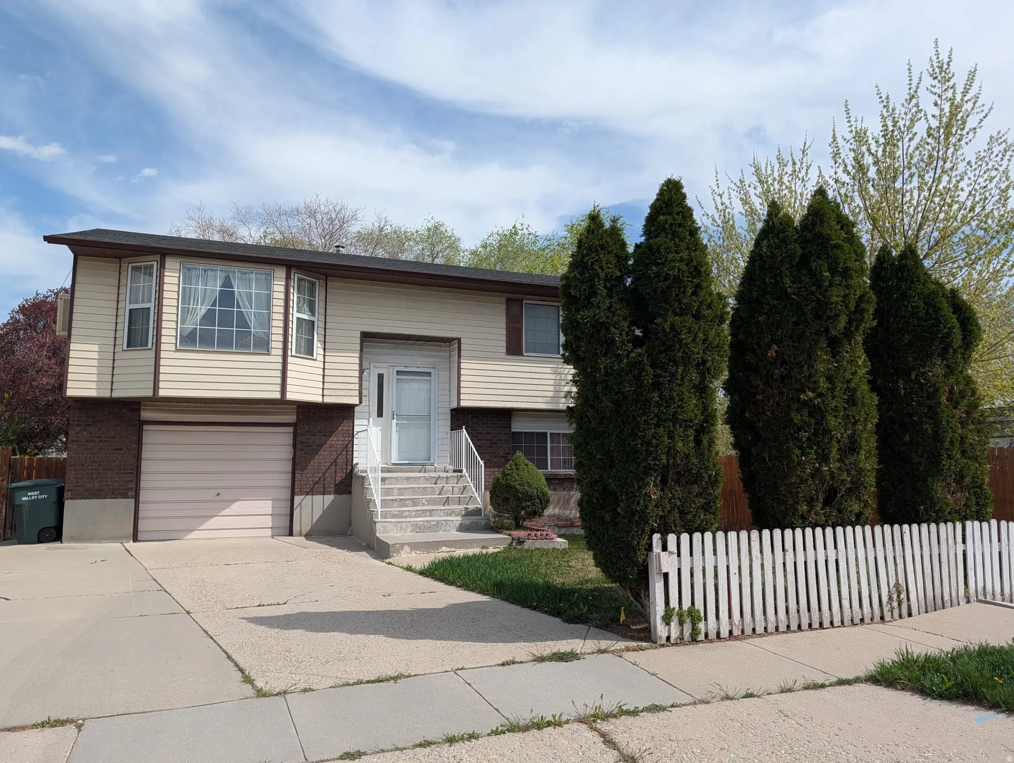 Bi-level home featuring brick siding, a fenced front yard, concrete driveway, and an attached garage