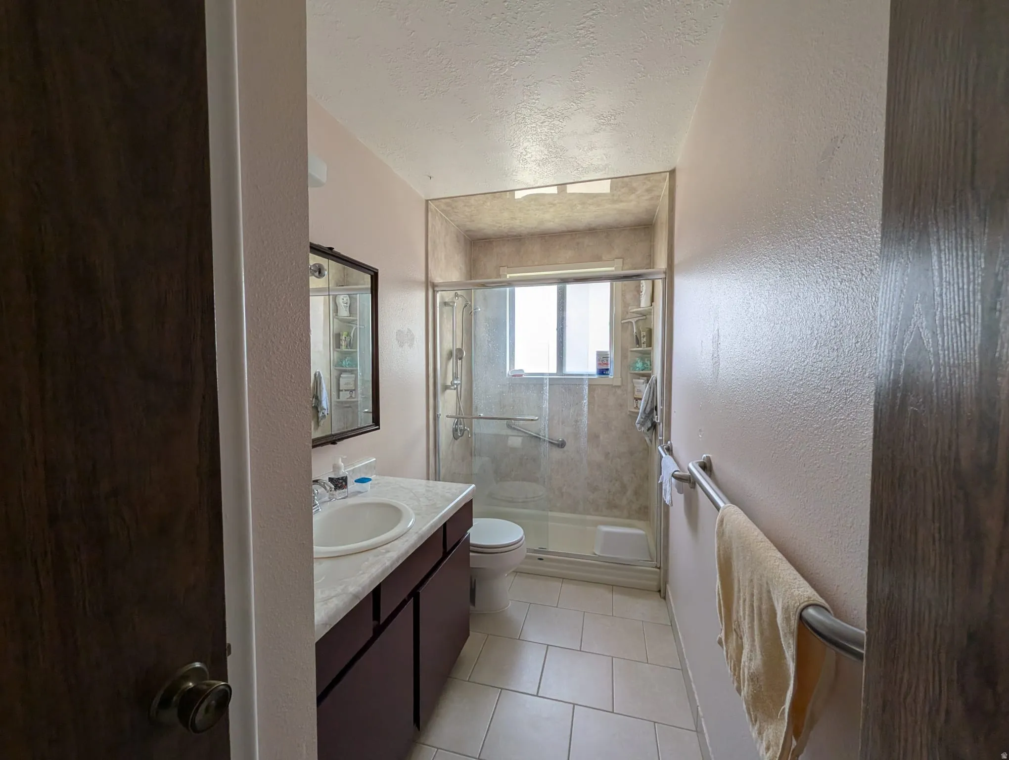 Full bathroom with a textured ceiling, a shower stall, vanity, a textured wall, and light tile patterned flooring