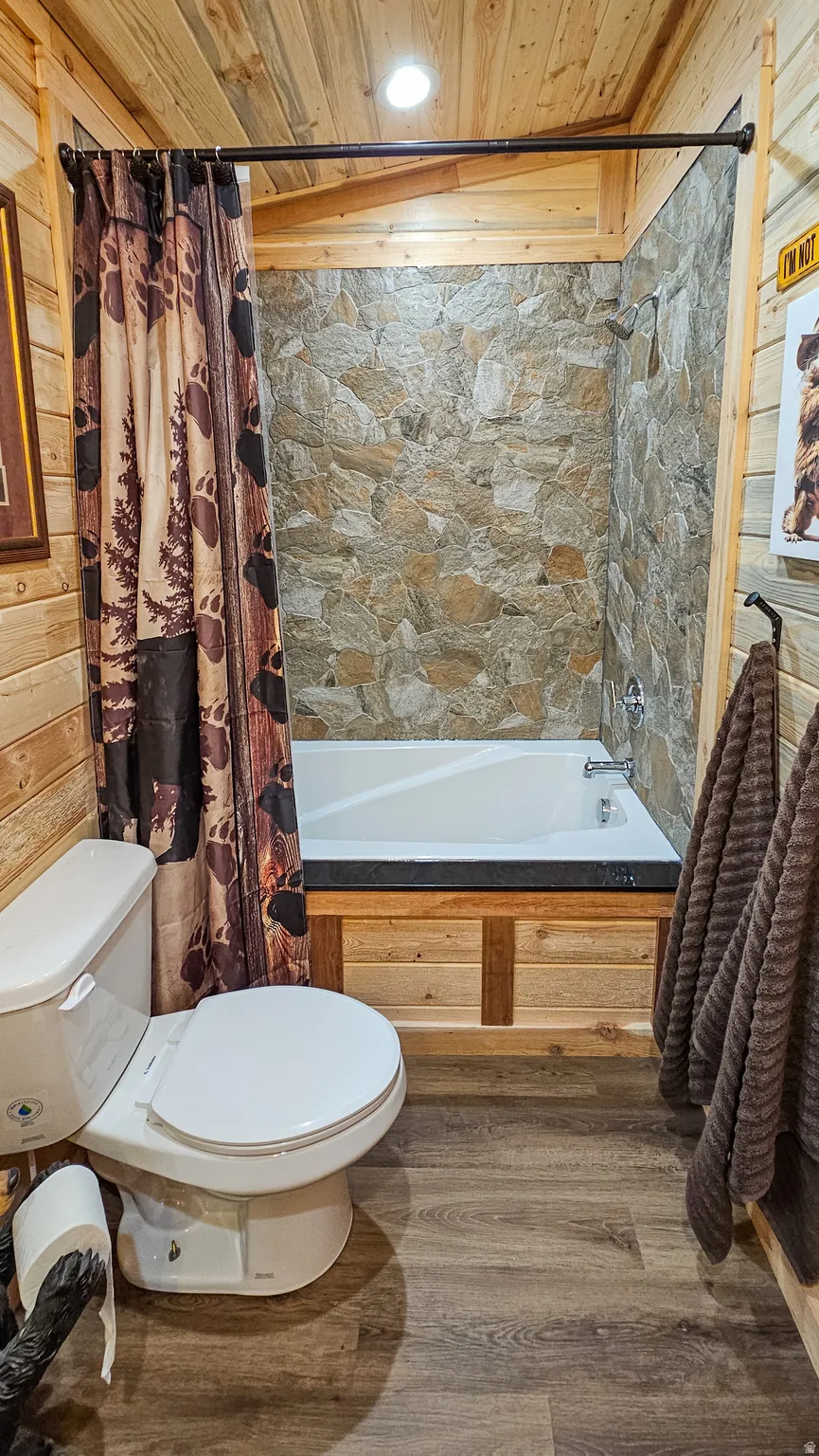 Bathroom featuring wood ceiling, dark wood-style floors, shower / tub combo, and wooden walls