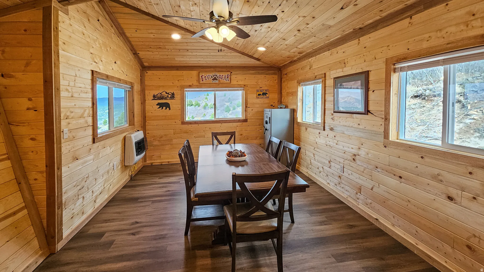 Dining area with wooden walls, dark wood-style floors, heating unit, ceiling fan, and a vaulted wood ceiling