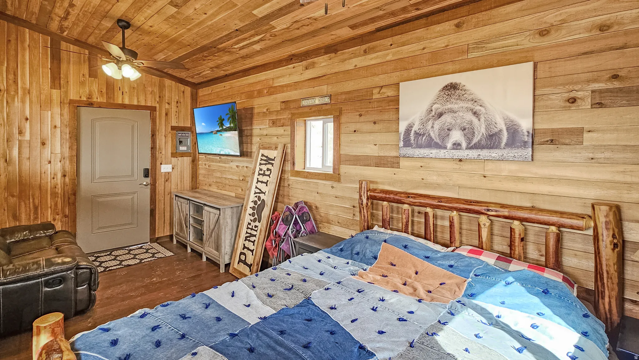 Guest Cabin Bedroom with wood walls, dark wood-style floors, wooden ceiling, and a ceiling fan