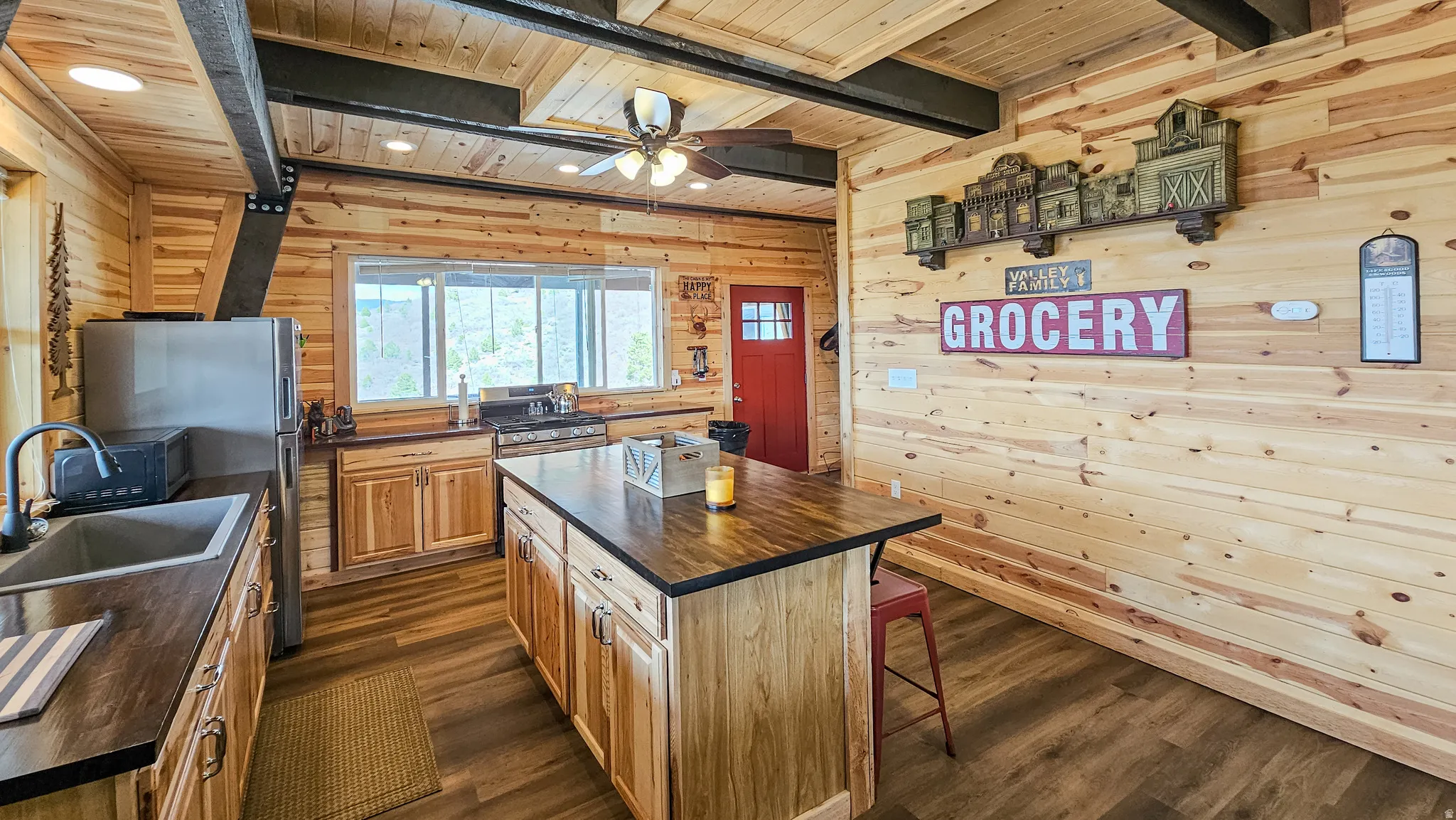 Kitchen featuring wooden walls, a wooden ceiling with exposed beams, a breakfast bar area, dark wood-style flooring, and a kitchen island