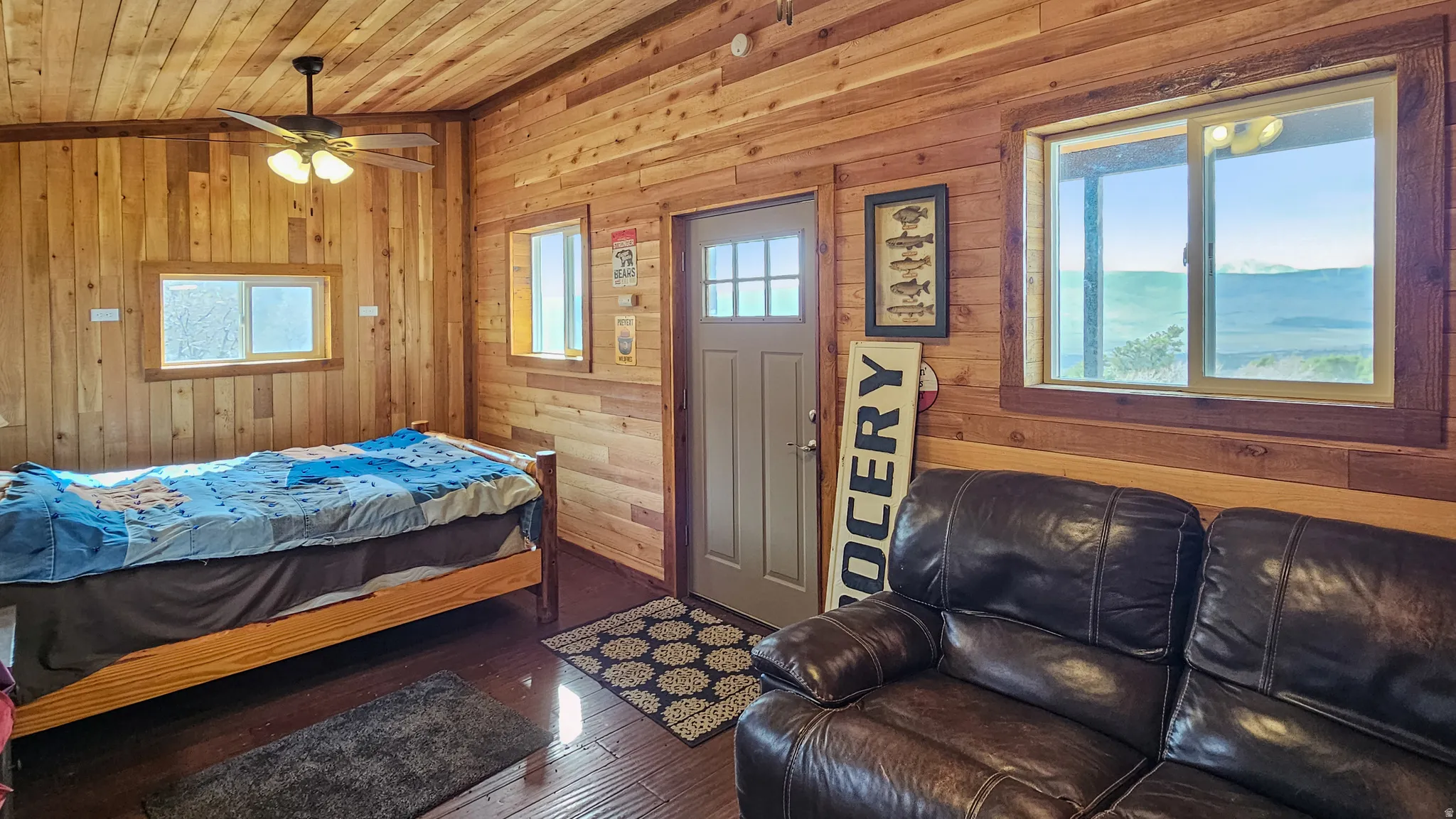 Guest Cabin Bedroom with multiple windows, wood walls, hardwood / wood-style flooring, wooden ceiling, and ceiling fan