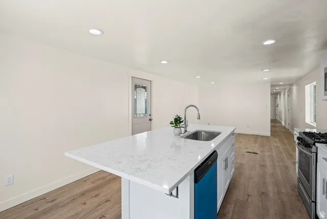 Kitchen featuring gas range, light stone countertops, light wood-type flooring, a kitchen island with sink, and dishwasher