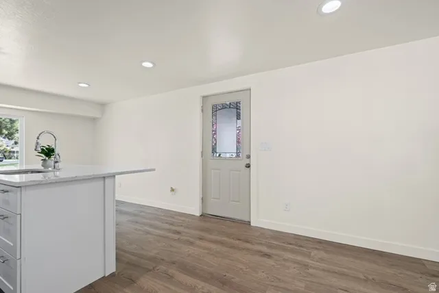 Kitchen featuring recessed lighting, dark wood-style flooring, a center island with sink, white cabinets, and light stone countertops