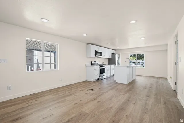 Kitchen featuring a center island with sink, white cabinets, stainless steel appliances, light countertops, and open floor plan
