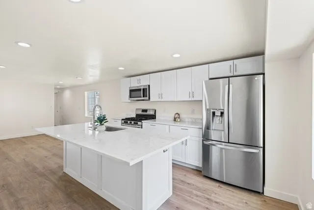 Kitchen with stainless steel appliances, white cabinets, light wood-style floors, light stone countertops, and recessed lighting