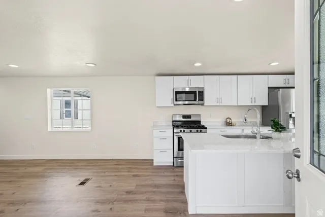 Kitchen featuring stainless steel appliances, white cabinets, light stone counters, light wood-style floors, and recessed lighting