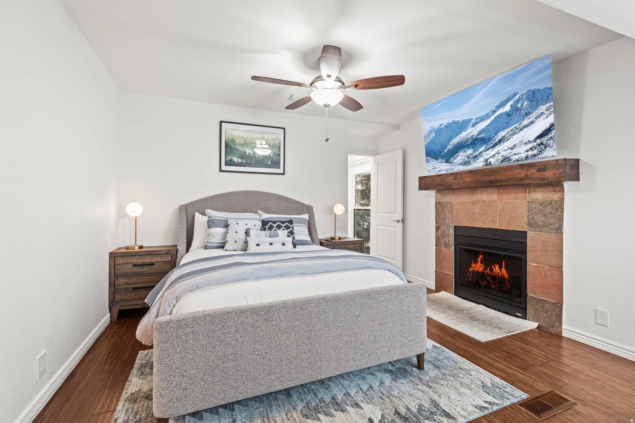 Bedroom with ceiling fan, a tiled fireplace, and dark wood finished floors