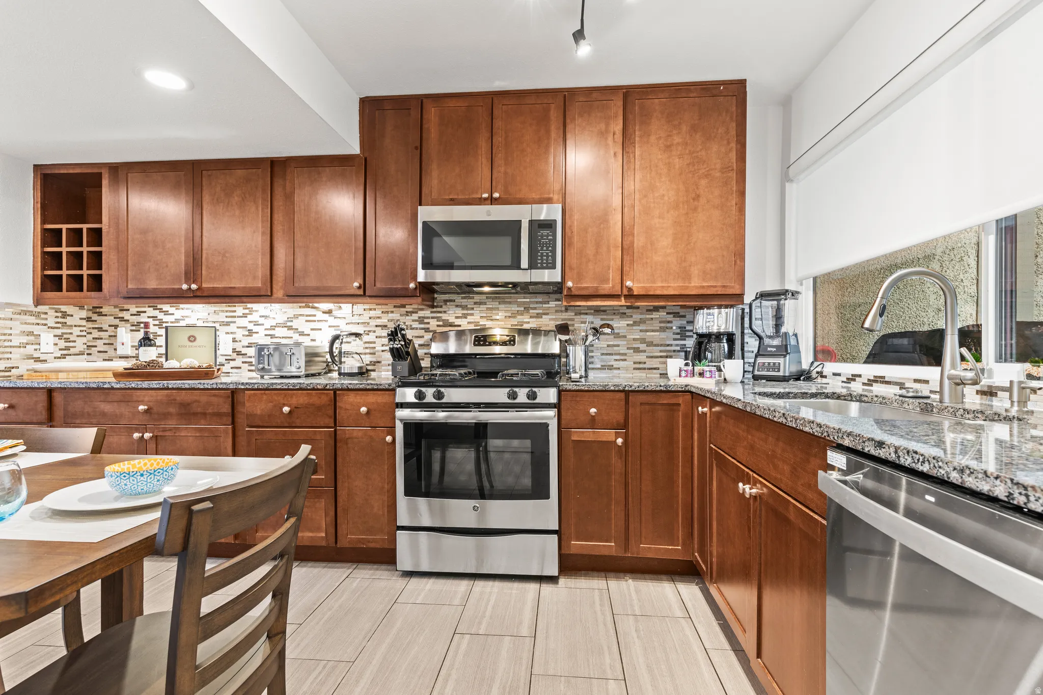 Kitchen with stainless steel appliances, light stone counters, backsplash, and wood finish cabinetry