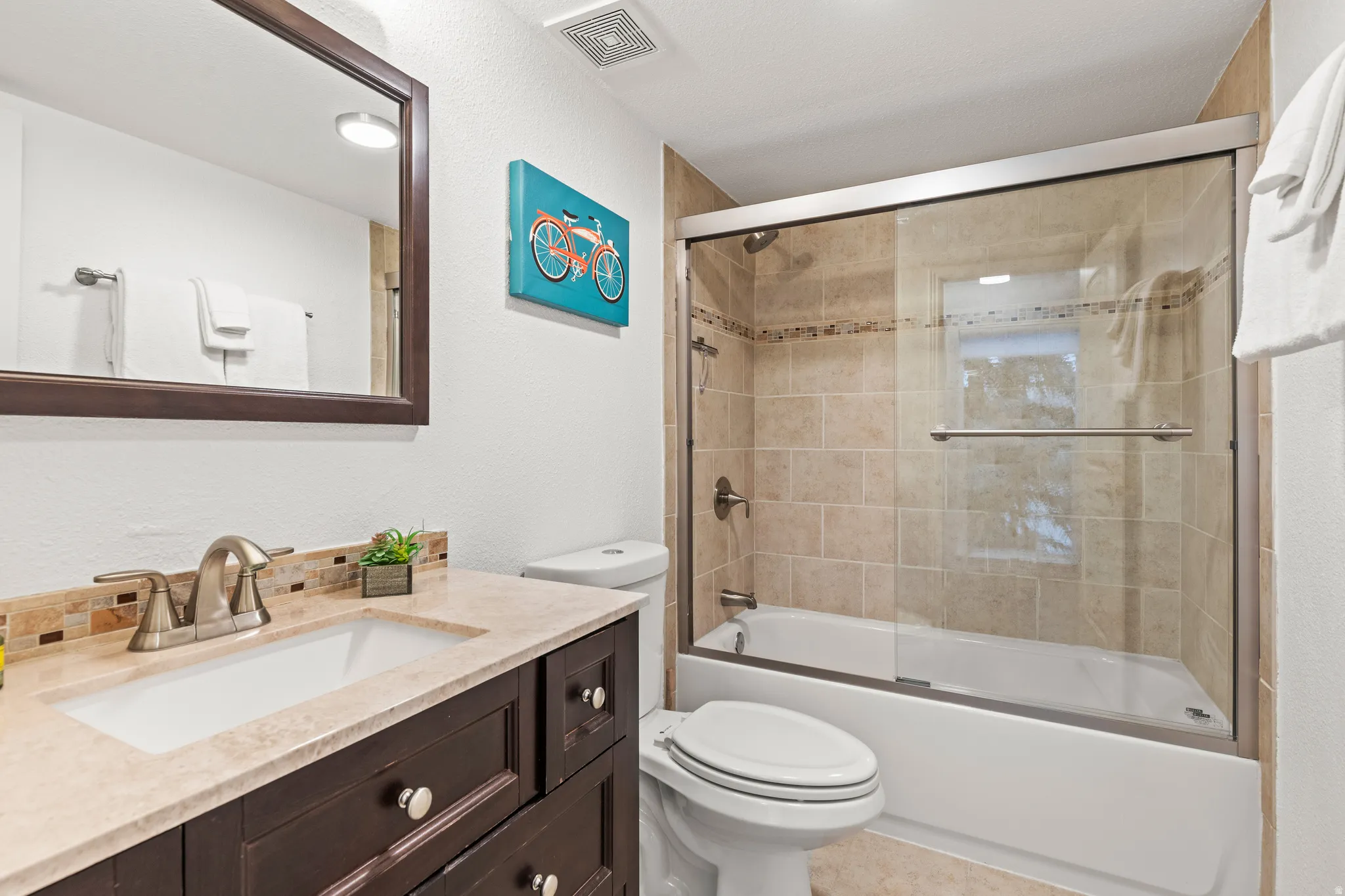 Full bath featuring vanity, enclosed tub / shower combo, and a textured wall