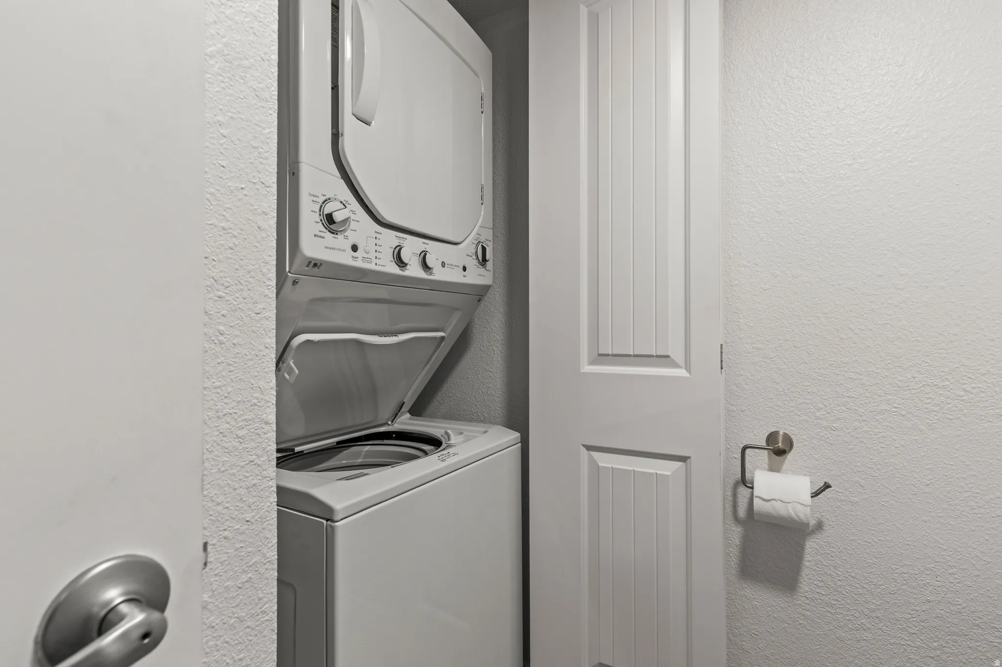 Laundry area featuring a textured wall and stacked washer / dryer