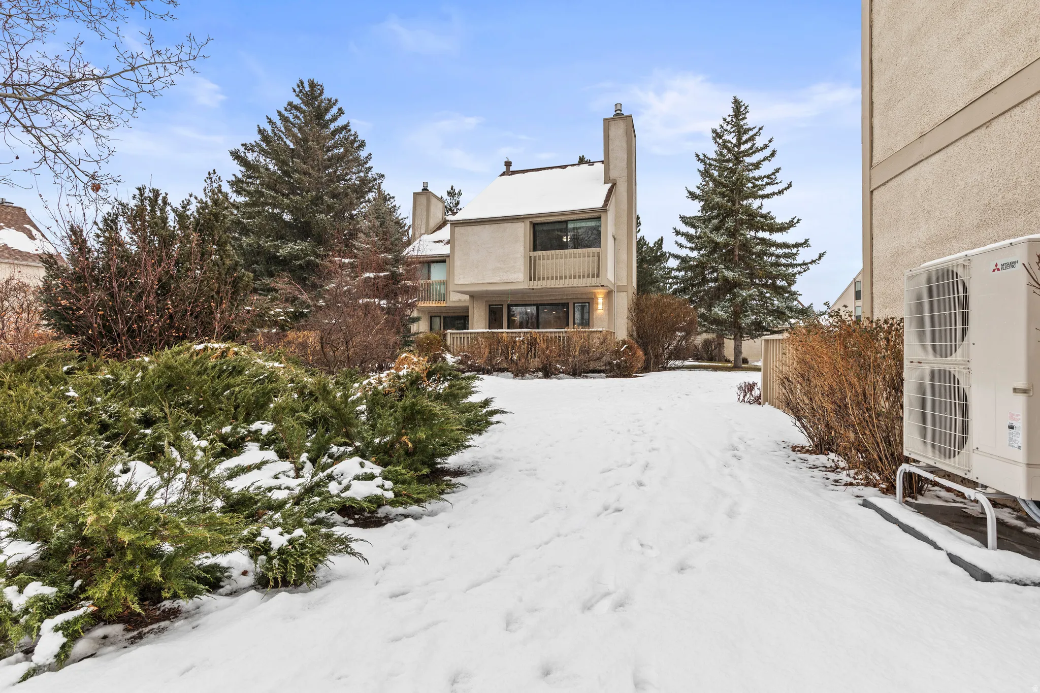 Snow covered house with a balcony, a chimney, and stucco siding