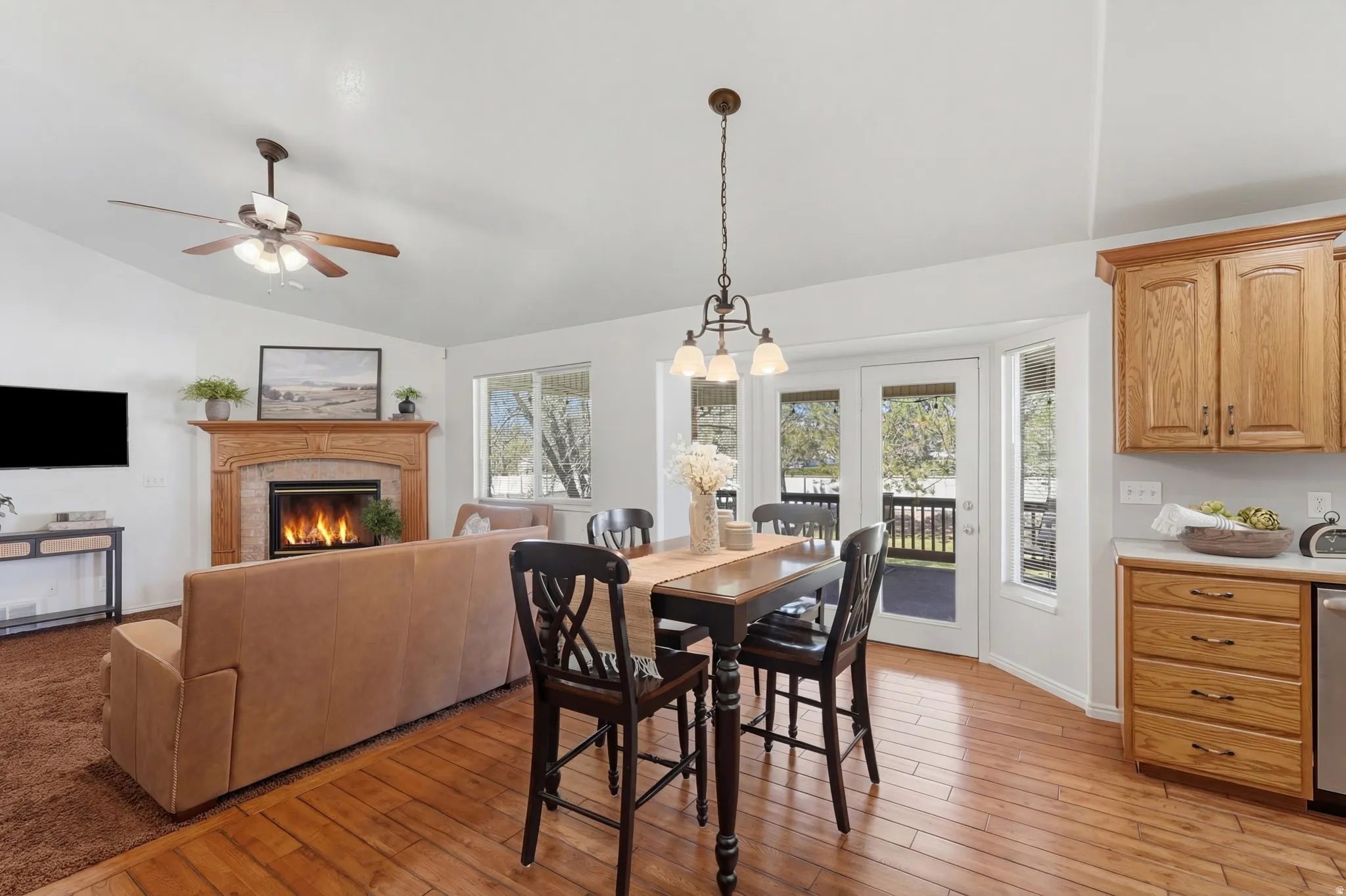 Dining area with light wood-style floors, ceiling fan, lofted ceiling, a fireplace, and hanging lights