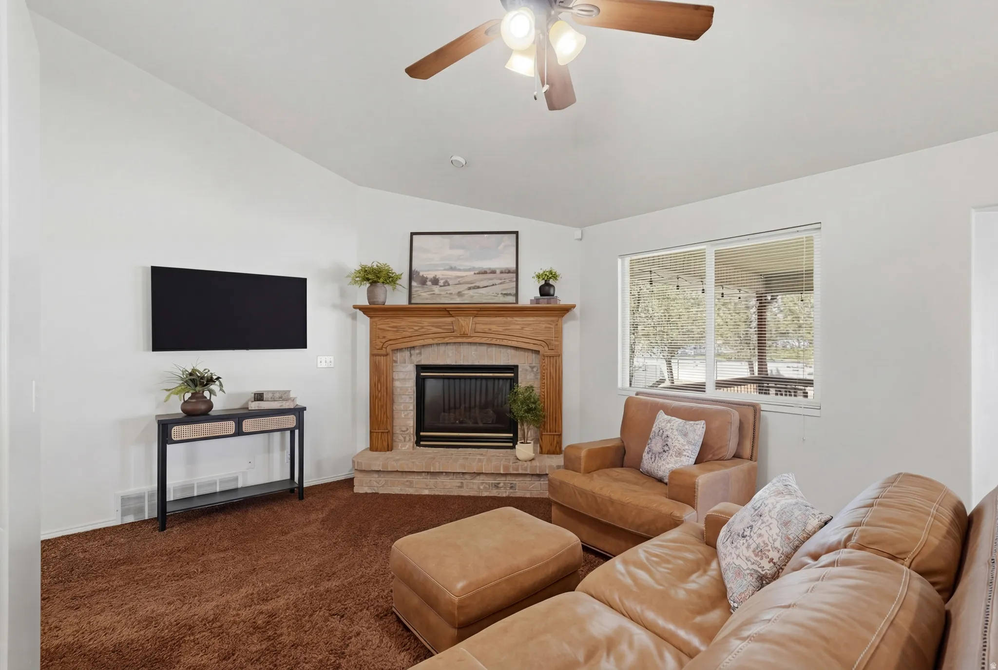 Living room featuring a brick fireplace, carpet, ceiling fan, and lofted ceiling