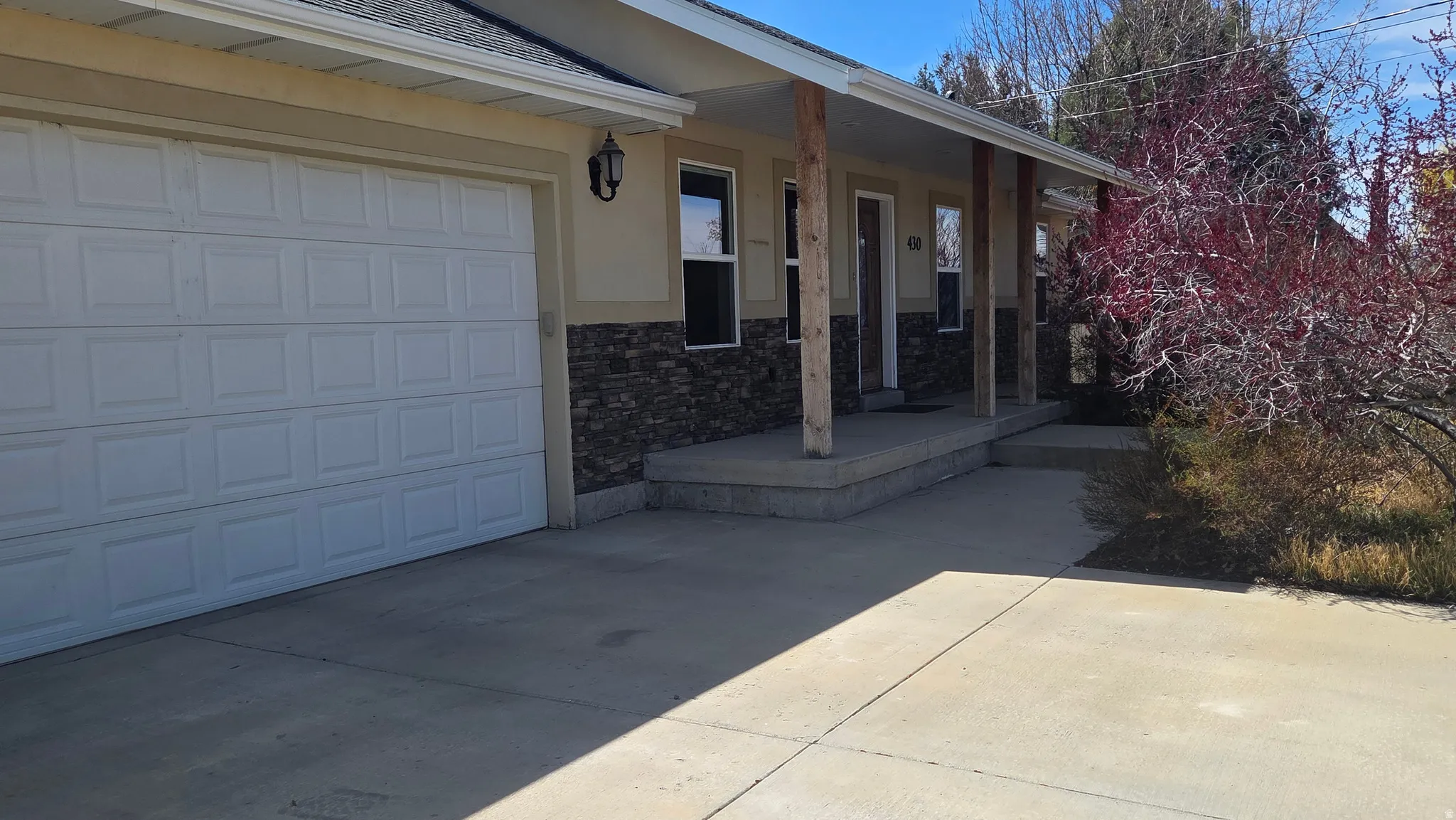 View of covered porch, stone siding, driveway, a garage, and stucco siding