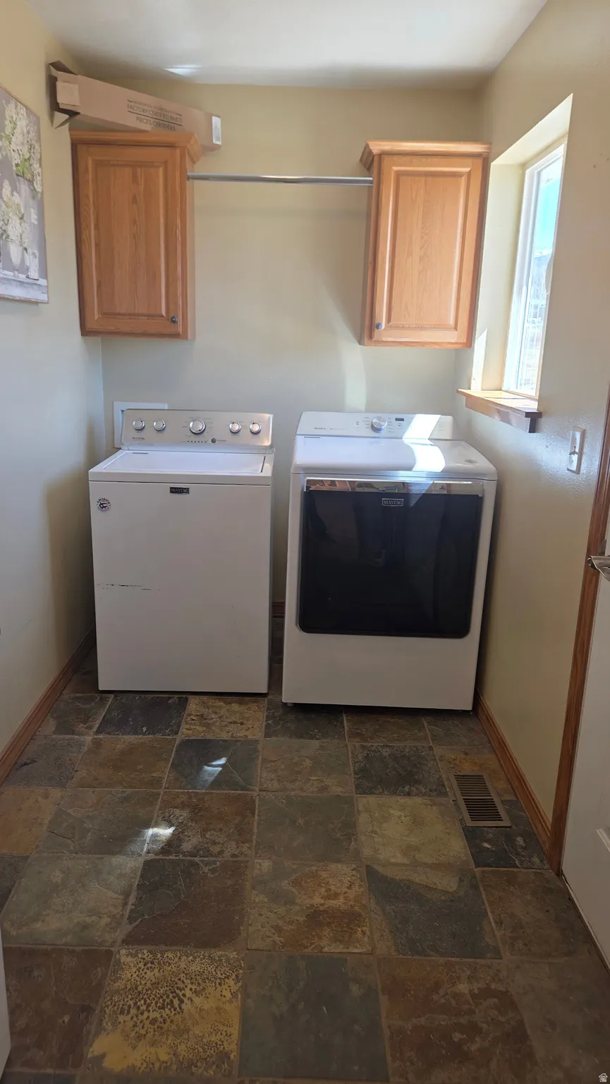 Laundry area featuring cabinet space, stone tile floors, and independent washer and dryer