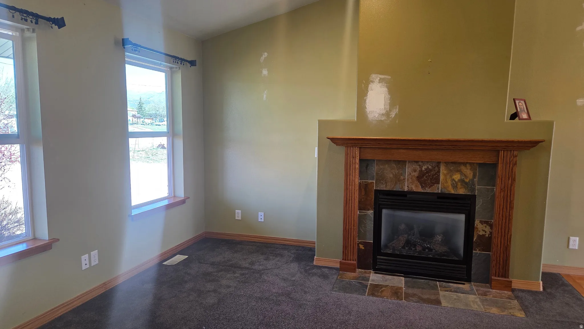 Unfurnished living room featuring a tiled fireplace and dark colored carpet