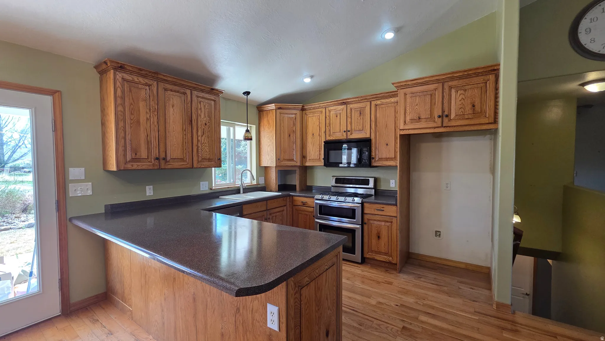Kitchen featuring wood finish cabinetry, dark countertops, range with two ovens, a peninsula, and lofted ceiling