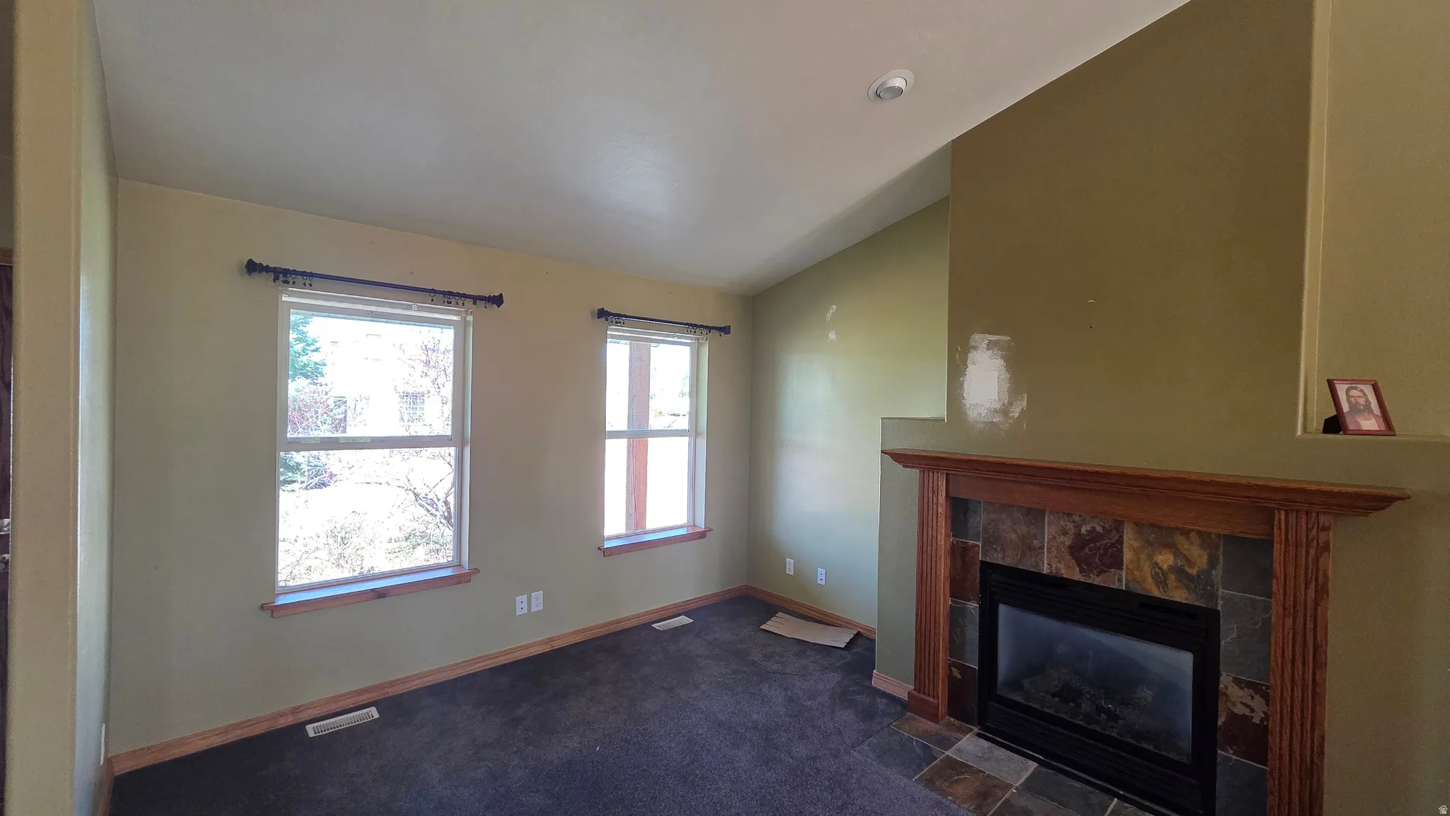 Unfurnished living room featuring vaulted ceiling, a tile fireplace, and dark colored carpet
