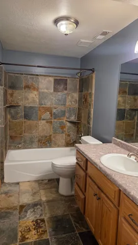 Bathroom #3 with stone tile flooring, vanity, shower / tub combination