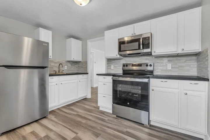 Kitchen featuring stainless steel appliances, white cabinetry, light wood finished floors, and backsplash