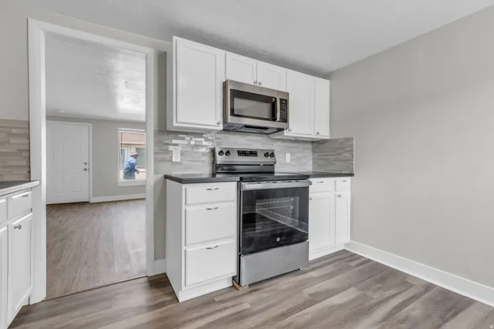 Kitchen with stainless steel appliances, white cabinets, backsplash, and light wood-type flooring