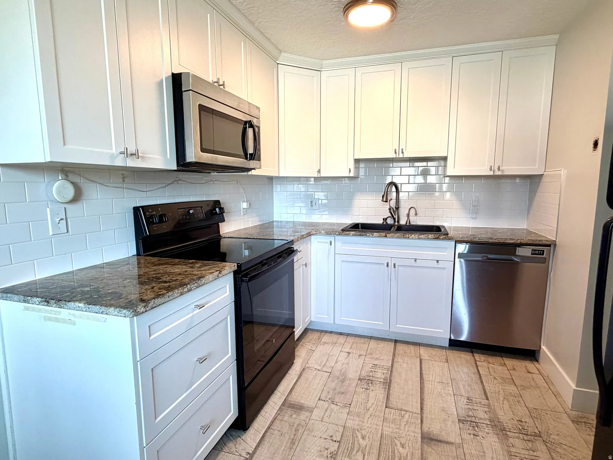 Kitchen featuring stainless steel appliances, dark stone counters, white cabinets, light wood-style floors, and backsplash