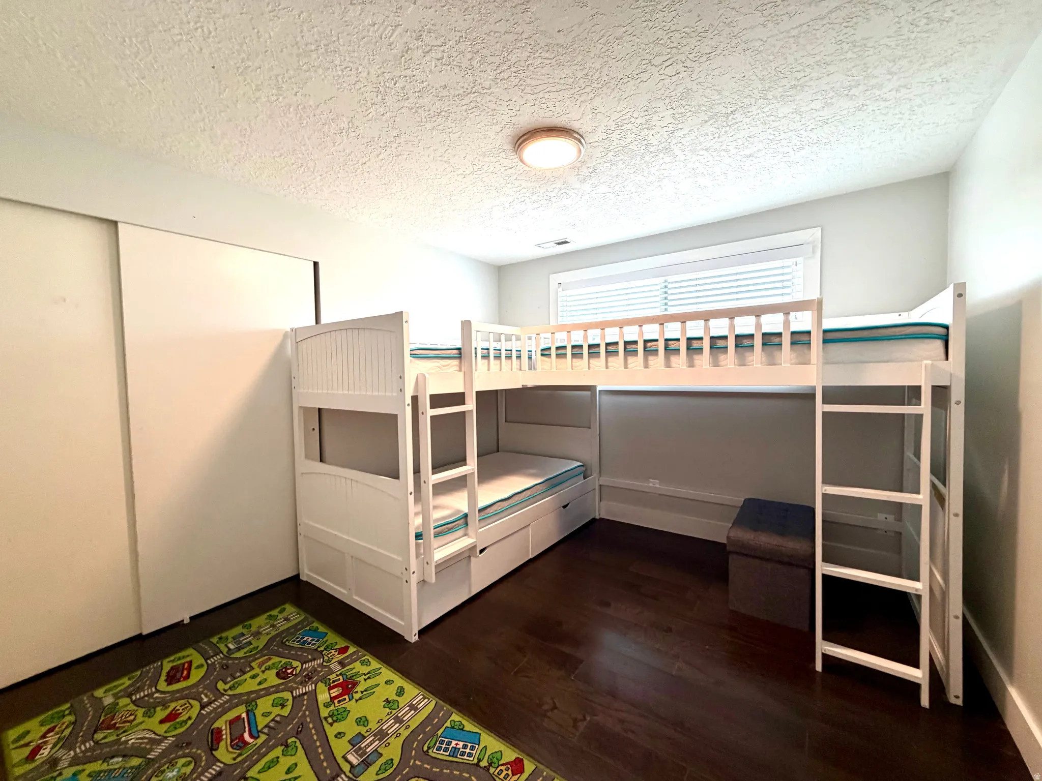 Unfurnished bedroom with a textured ceiling, dark wood-style floors, and a closet