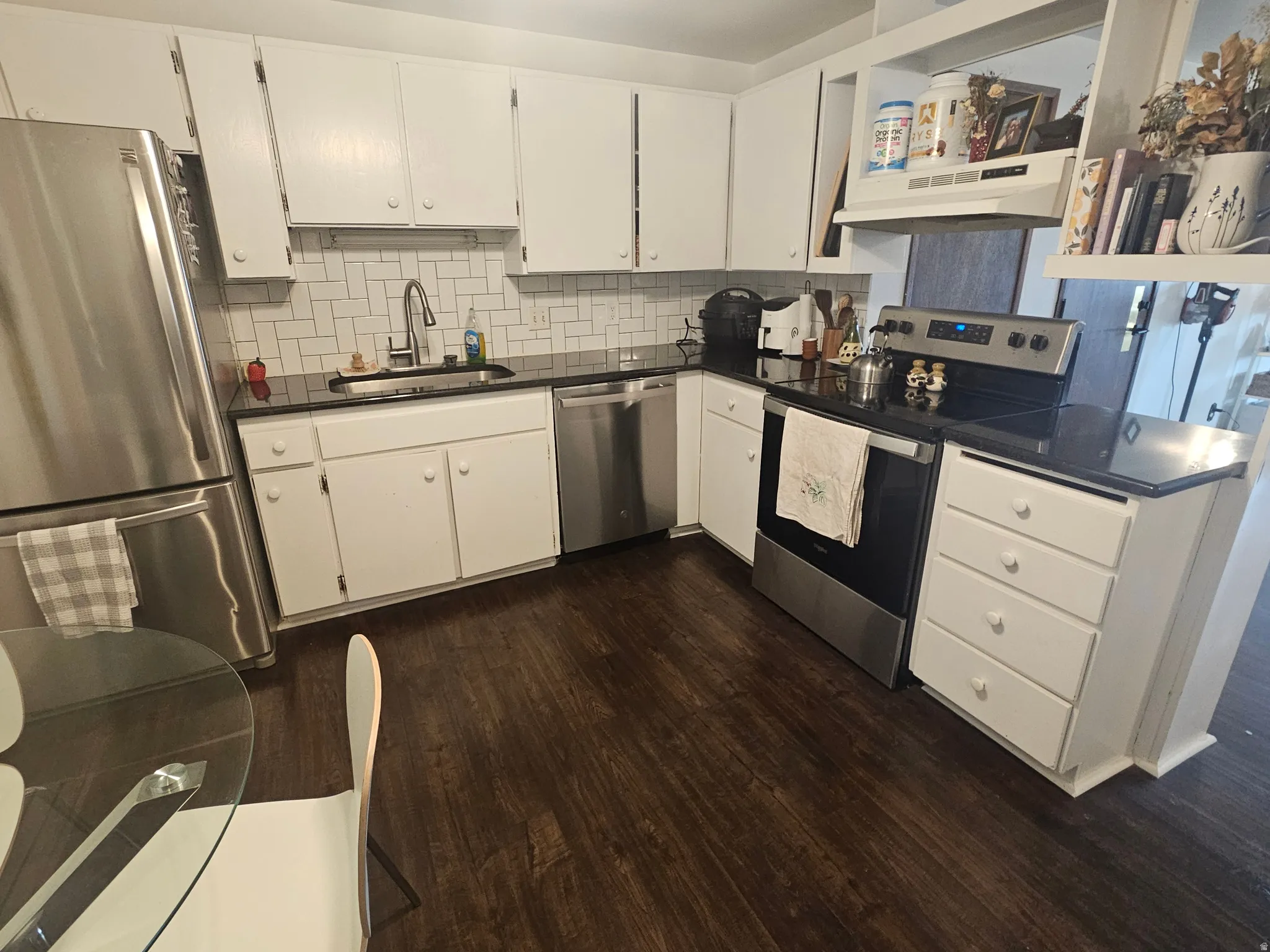 Kitchen with white cabinets, stainless steel appliances, tasteful backsplash, and dark wood-style flooring