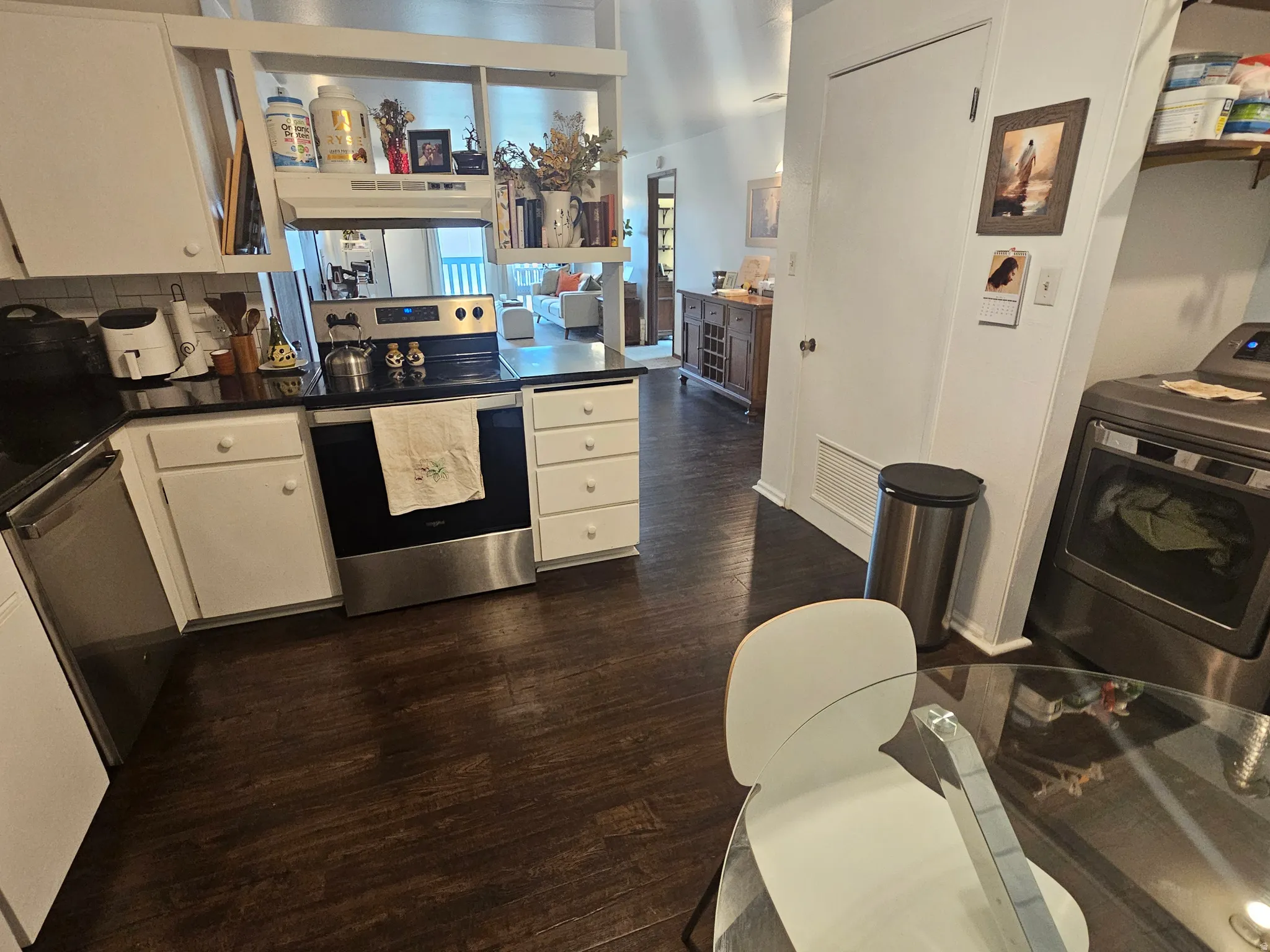 Kitchen with white cabinets, stainless steel appliances, washer / dryer, dark wood-type flooring, and open shelves