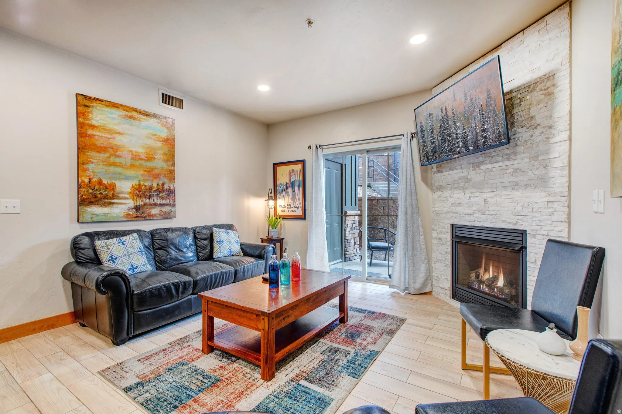 Living area with light wood finished floors, a stone fireplace, and recessed lighting