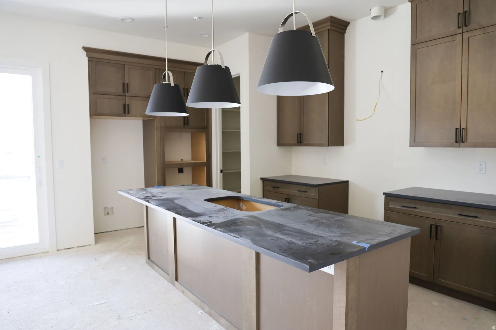 Kitchen featuring an island with sink, wood finish cabinetry, and decorative light fixtures