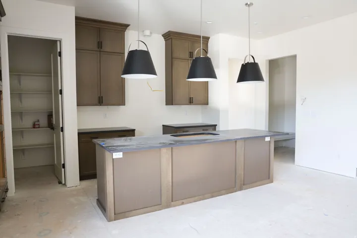 Kitchen featuring a kitchen island with sink, decorative light fixtures, wood finish cabinets, and concrete floors