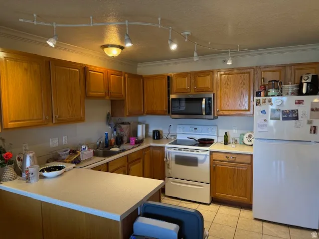 Kitchen with wood finish cabinets, white appliances, light countertops, a peninsula, and a textured ceiling