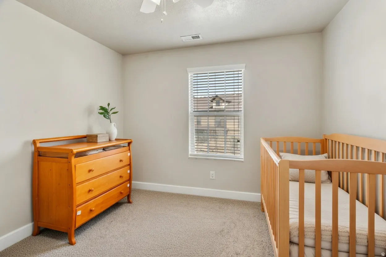 Bedroom featuring light carpet, a ceiling fan, and a nursery area