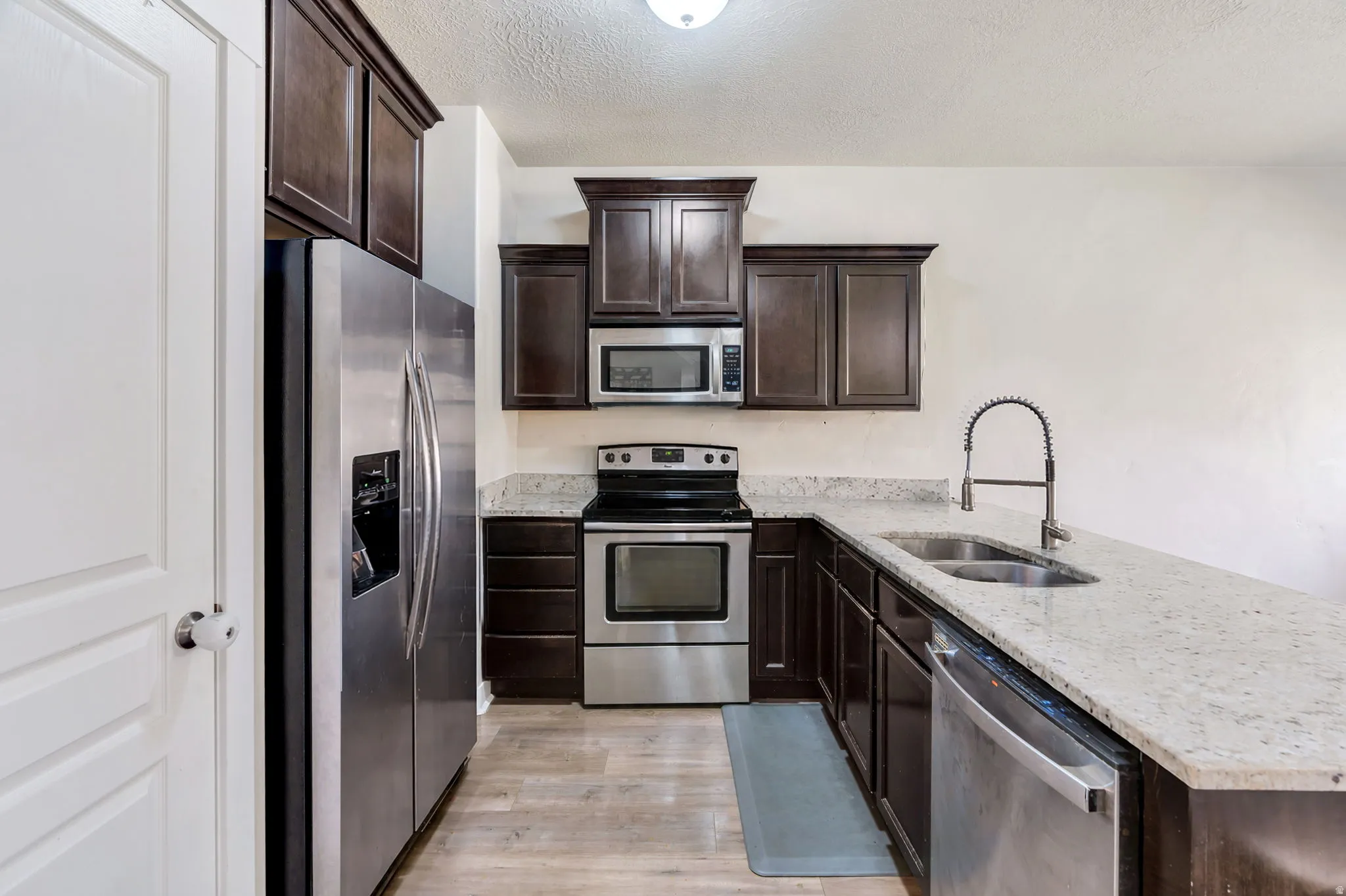 Kitchen featuring dark wood finish cabinets, stainless steel appliances, light stone counters, a peninsula, and a textured ceiling