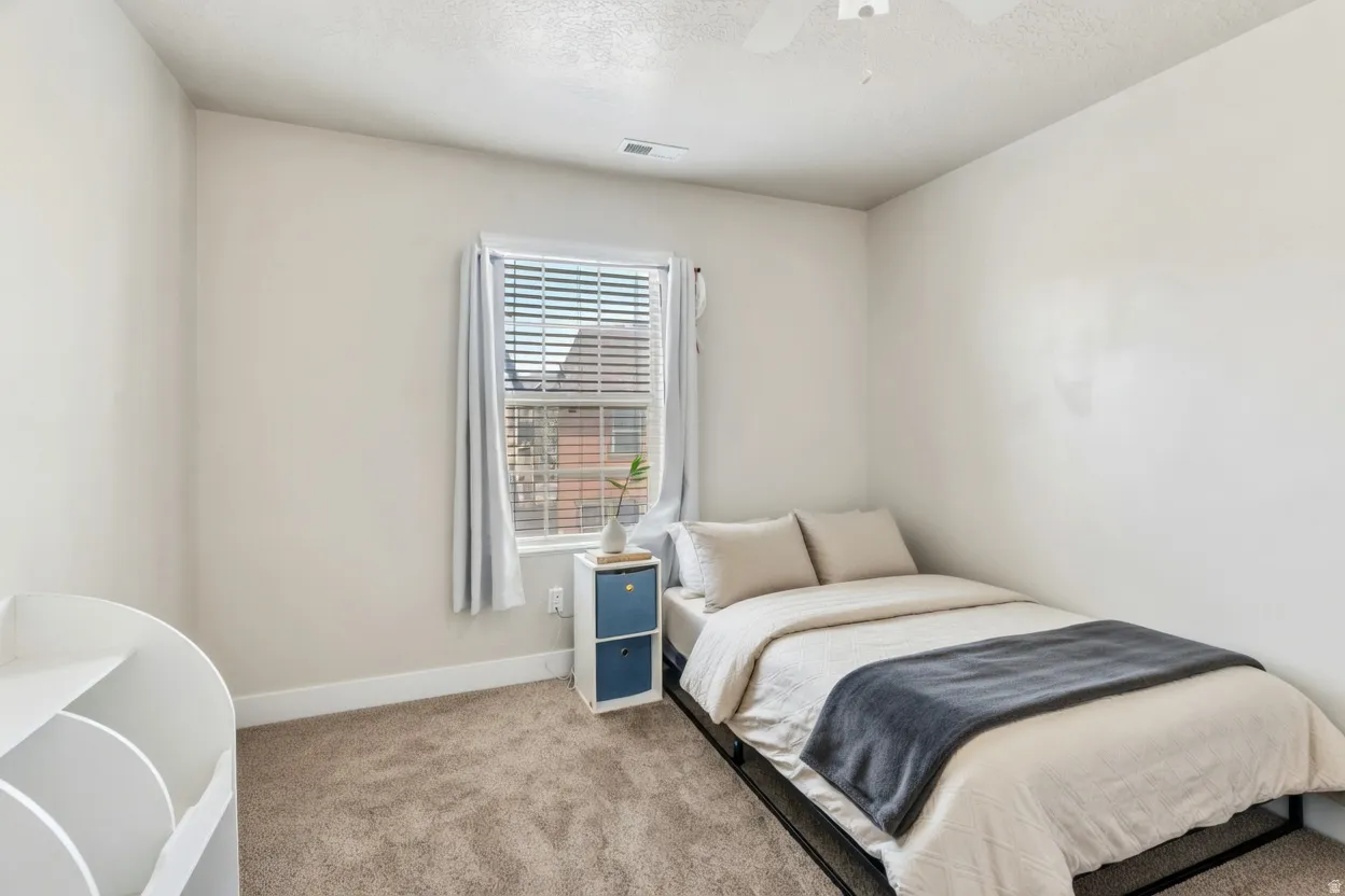 Bedroom with light colored carpet, ceiling fan, and a textured ceiling