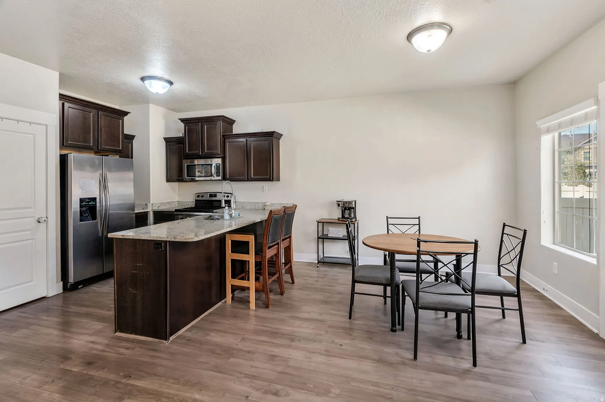 Kitchen with dark wood finish cabinetry, stainless steel appliances, light stone counters, a peninsula, and light wood-type flooring