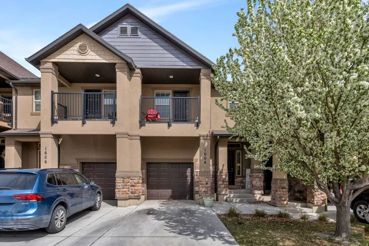 View of front of home with an attached garage, stucco siding, driveway, stone siding, and a balcony