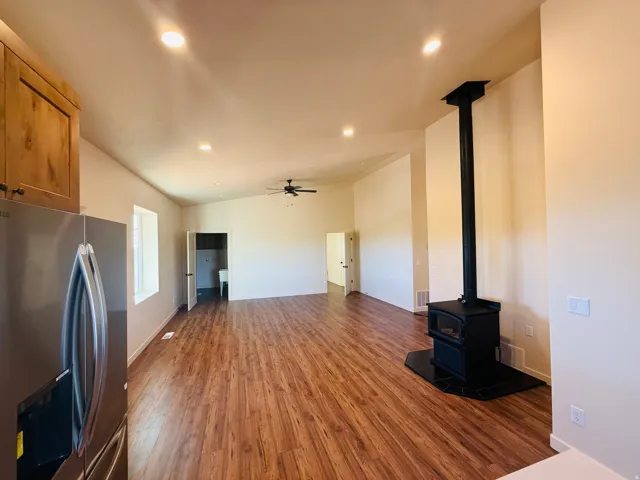 Unfurnished living room featuring dark wood-style floors, ceiling fan, recessed lighting, a wood stove, and lofted ceiling
