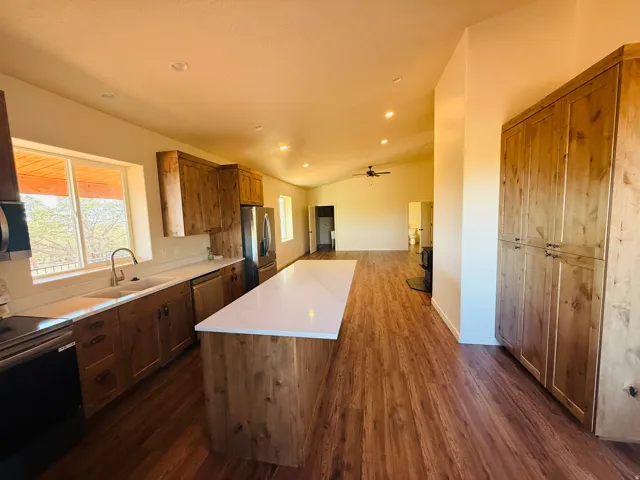 Kitchen featuring stainless steel appliances, a center island, vaulted ceiling, light countertops, and dark wood finished floors