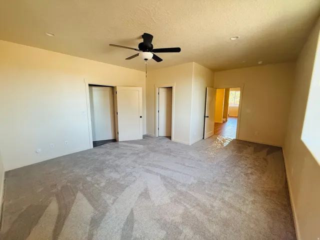 Master with light colored carpet, ceiling fan, a textured ceiling, bath and closet