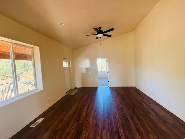 Unfurnished living room with dark wood-type flooring, vaulted ceiling, and ceiling fan